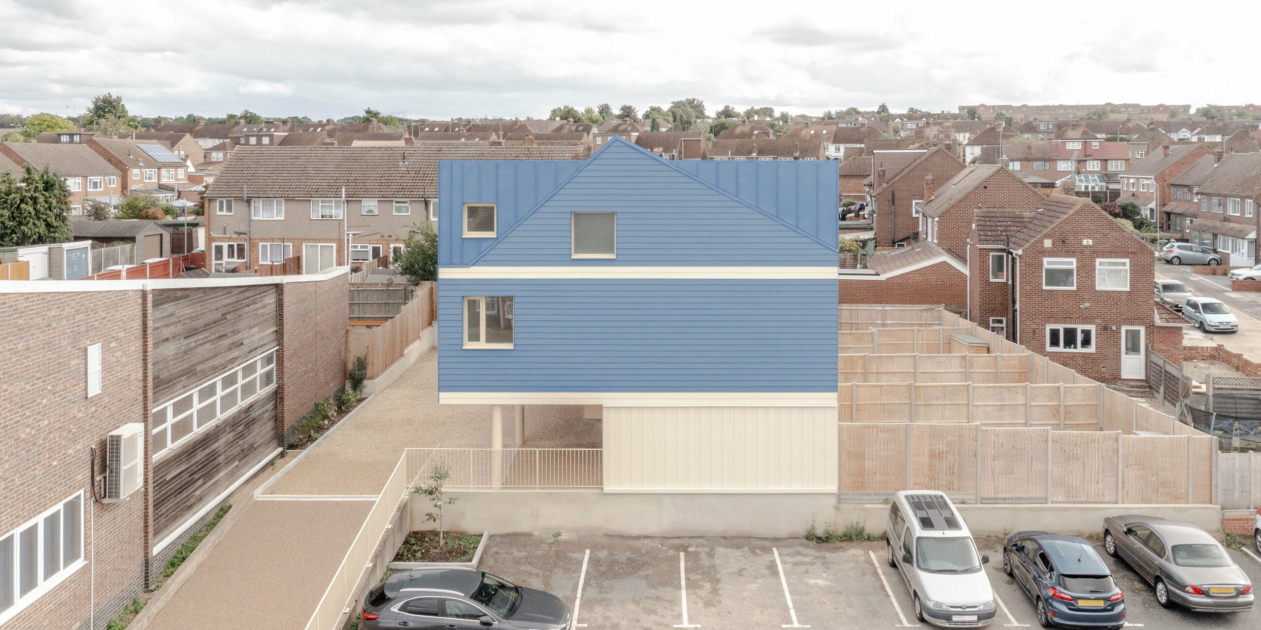 The photograph shows the Goldsmith Mews terraced housing complex from an elevated perspective, with the striking dusty blue FALZONAL standing seam roof and façade design from PREFA immediately catching the eye. The clear fold lines and uniform structure give the building a modern, precise look that stands out from the surrounding buildings. The light-coloured base area adds to the overall lightness. The robust, colour-stable PREFA aluminium guarantees lasting weather protection and enables a durable, architecturally expressive design.