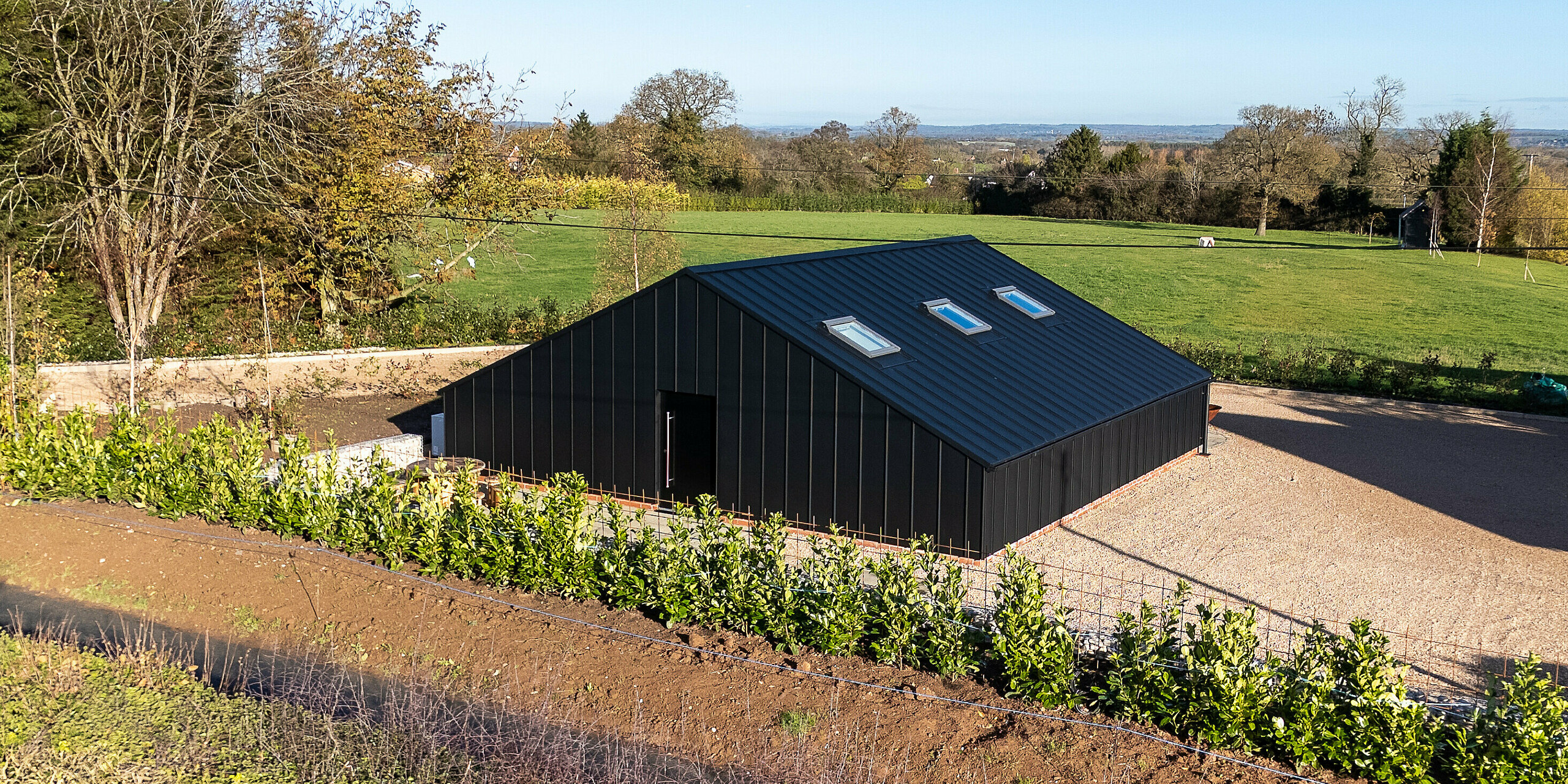 Rear view of the modern leisure building clad entirely with PREFA aluminum and a PREFALZ roof in P.10 black. The clean geometric form and seamless metal surface create a striking contrast with the surrounding landscape. The durable, weather‑resistant aluminum construction ensures long‑lasting protection and a premium architectural appearance.