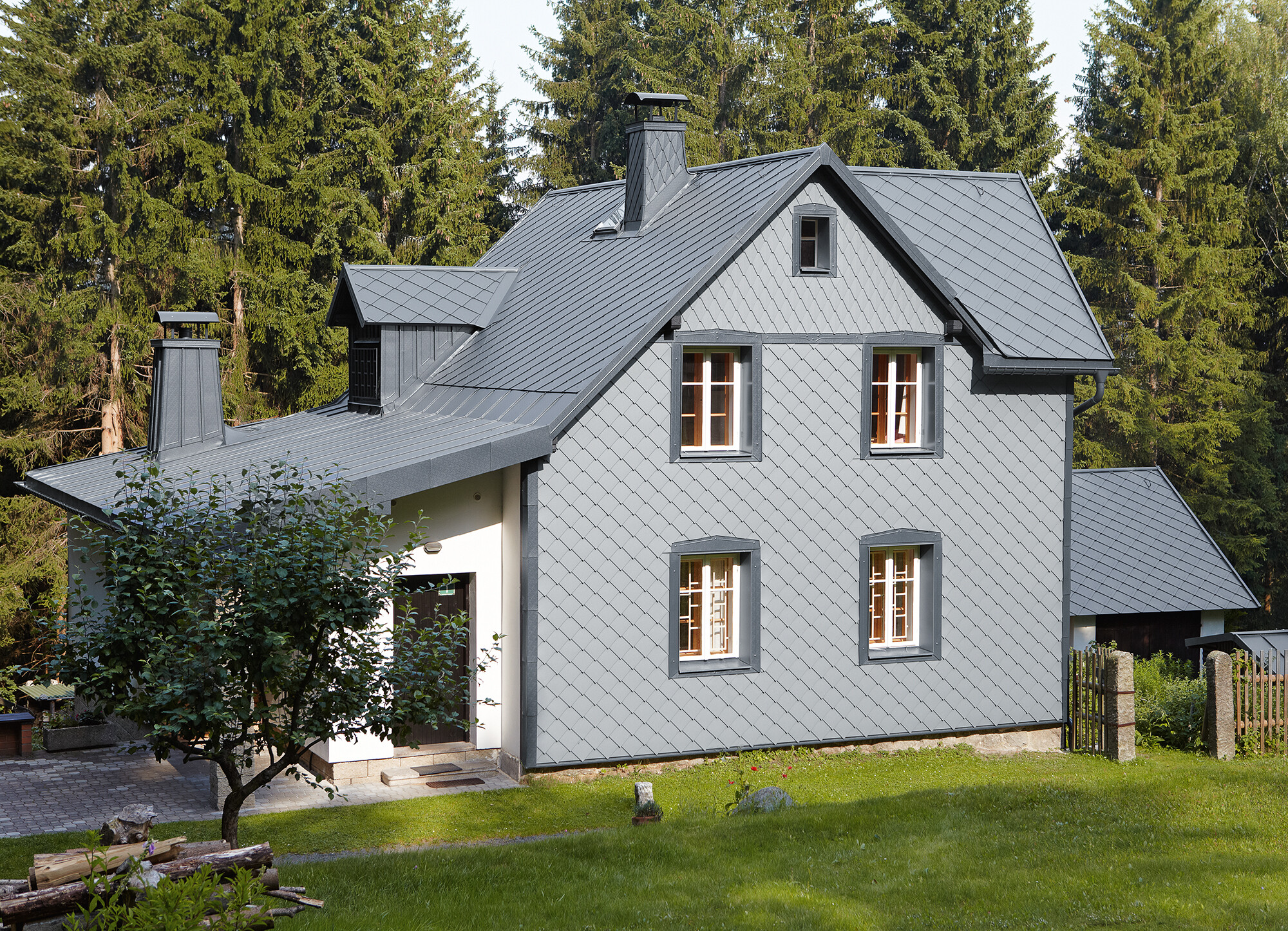 Façade with PREFA rhomboid façade tile 29 × 29 in light grey on the side of a building that faces the direction of the prevailing weather Detached house in a wooded area with a weather-resistant PREFA aluminium façade in light grey.