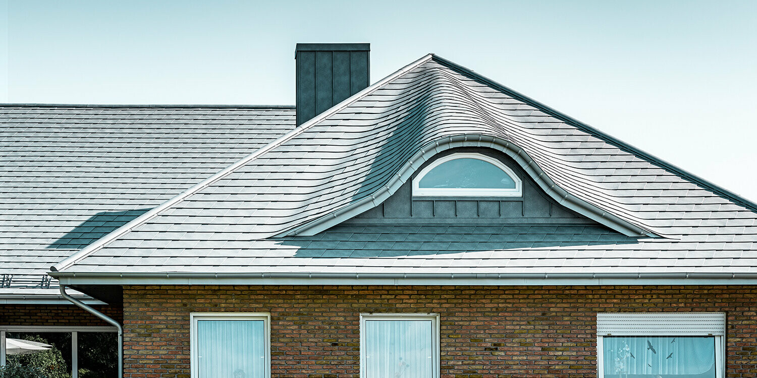 Detached house from the 70s with an aluminium shingle roof in P.10 stone grey with curved dormer with round window