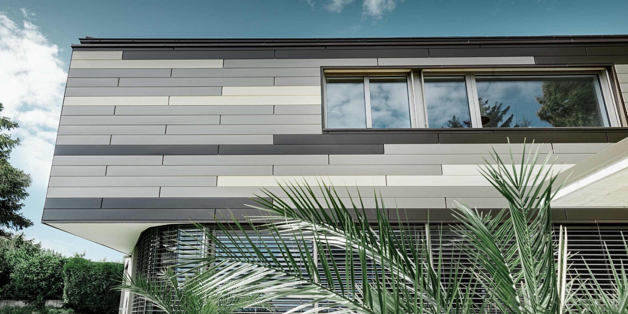 Modern detached house with a flat roof and covered terrace with an individually designed PREFA aluminium façade made of sidings in brown, bronze and ivory