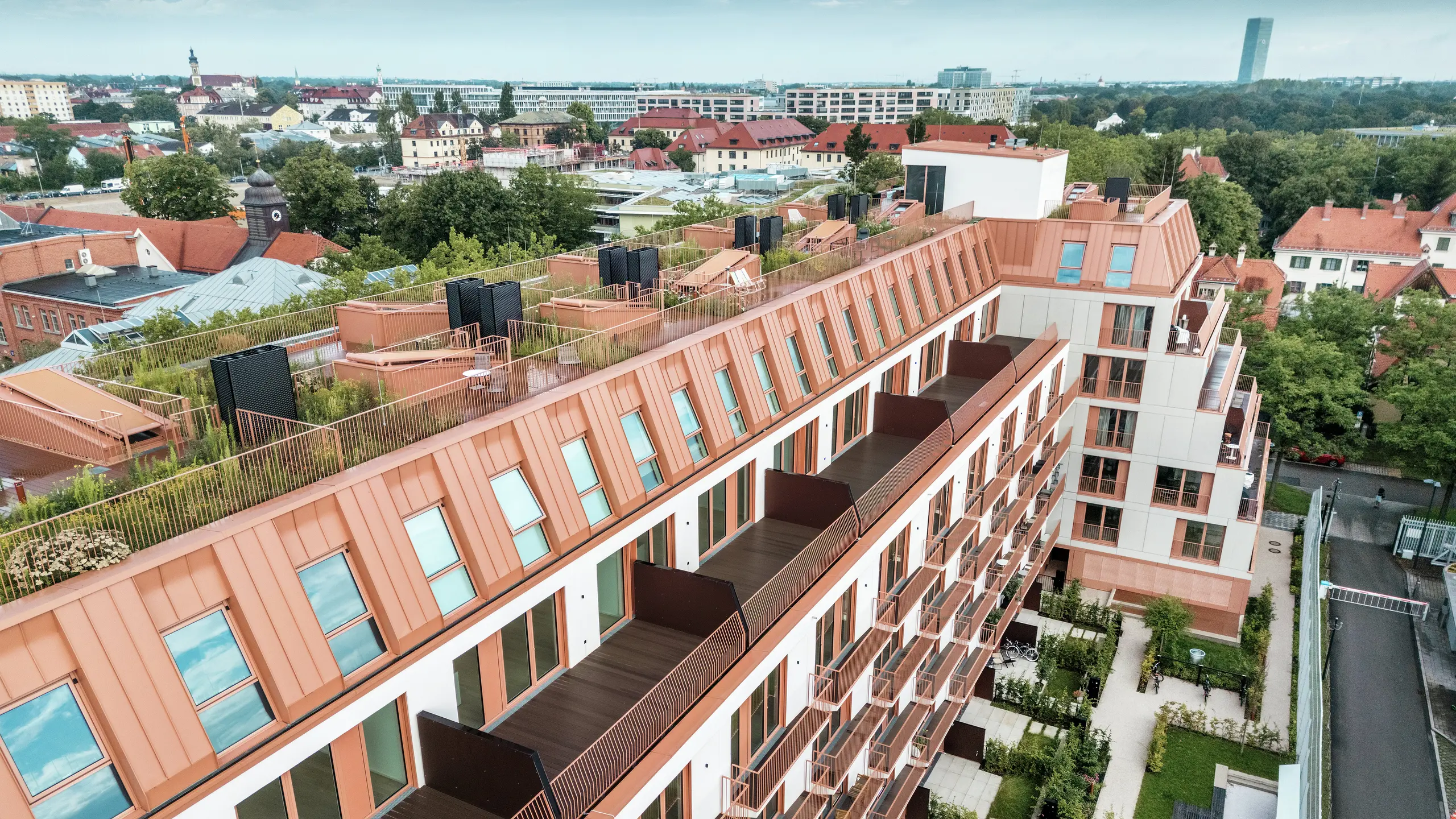 Aerial view of the Van B residential project in Munich with the striking PREFALZ aluminium roof in the special colour IGP Orange HDP from PREFA. Spacious balconies, green roof terraces and a precise façade design underline the well thought-out architectural concept. Ideal for sustainable urban development and urban living with a high quality of life and aesthetic appeal.