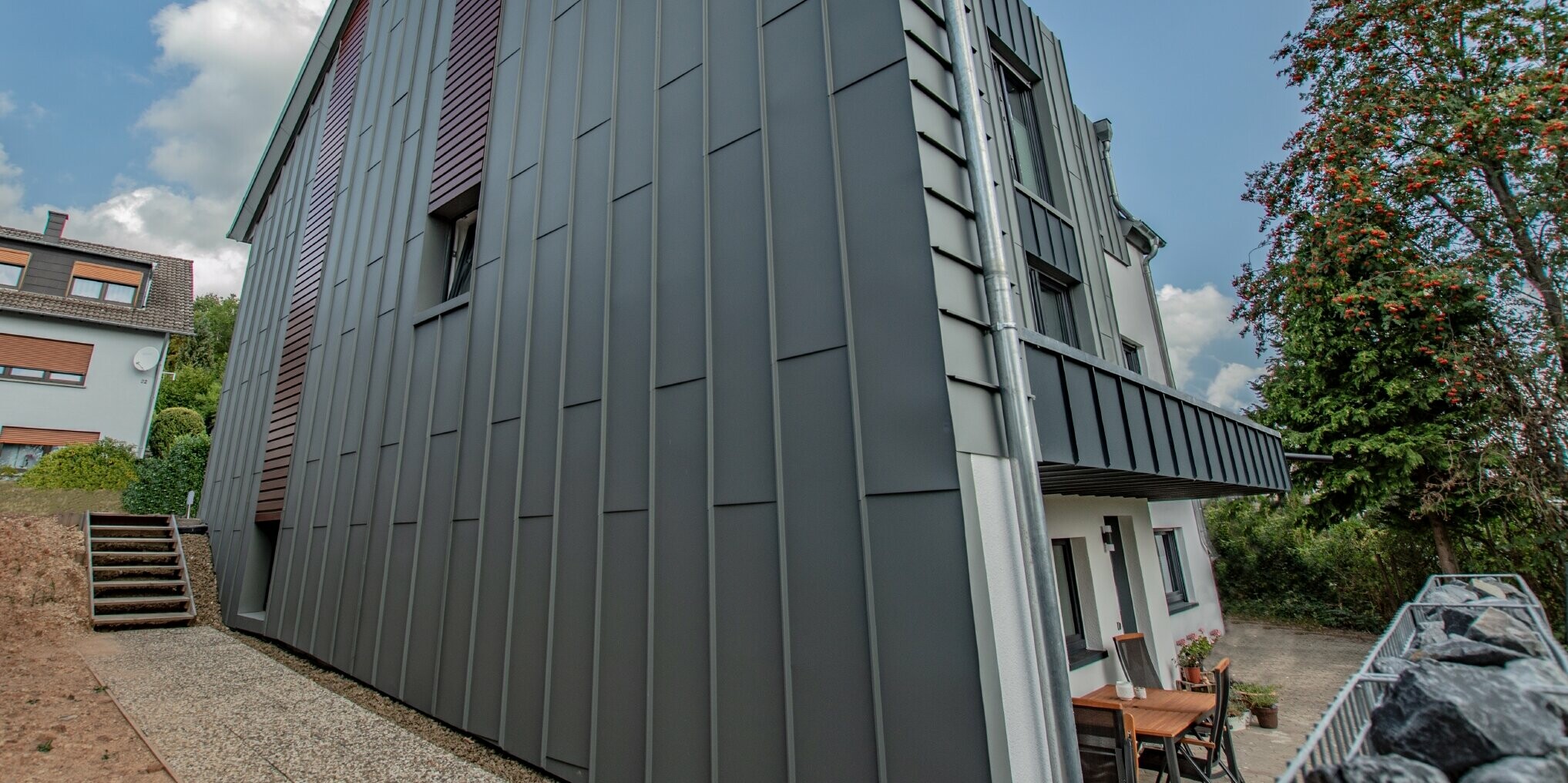 Façade design with vertical angular standing seam façade in light grey and horizontally installed façade panels in a dark wood finish. The entire façade was manufactured from PREFA aluminium.