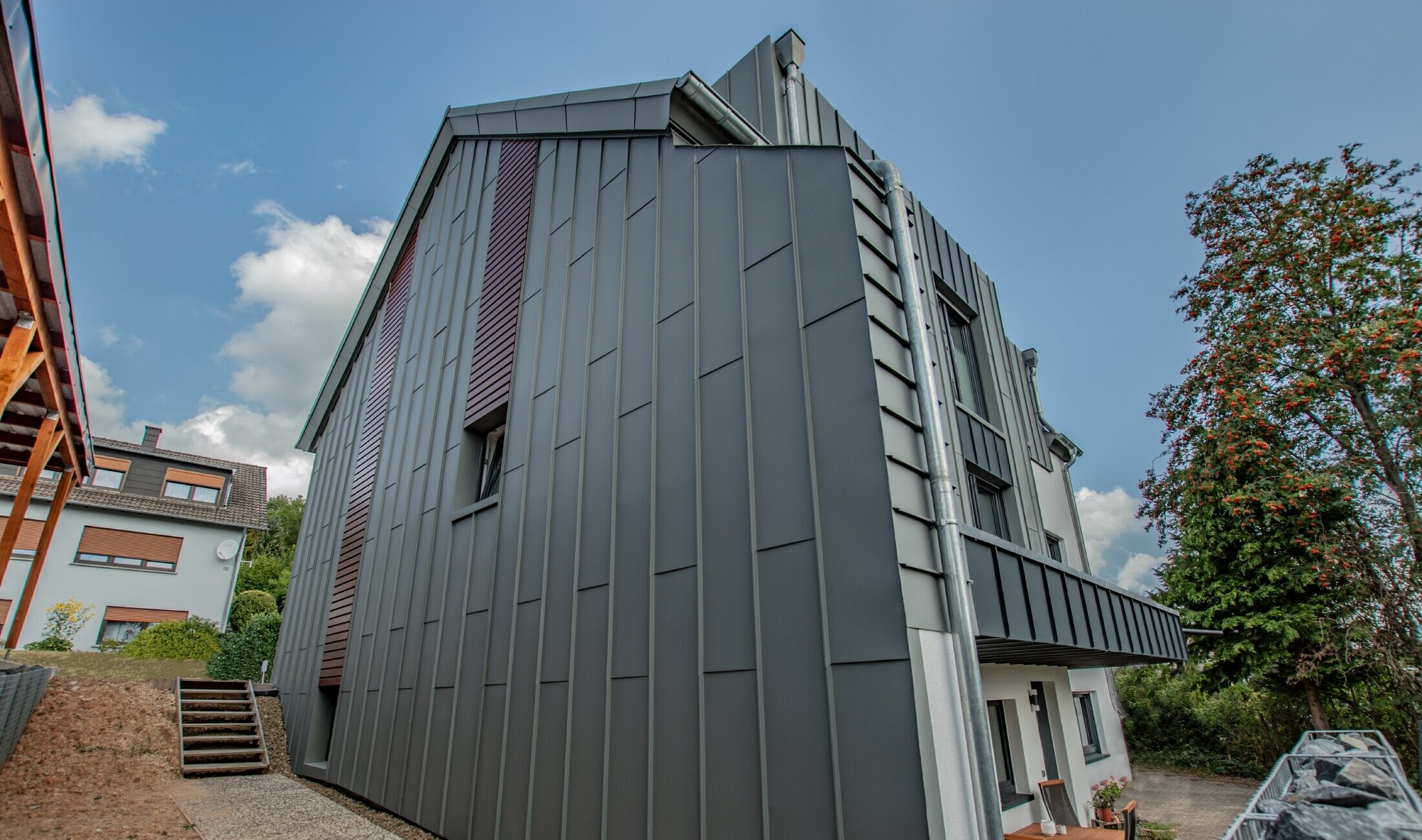 Façade design with vertical angular standing seam façade in light grey and horizontally installed façade panels in a dark wood finish. The entire façade was manufactured from PREFA aluminium.