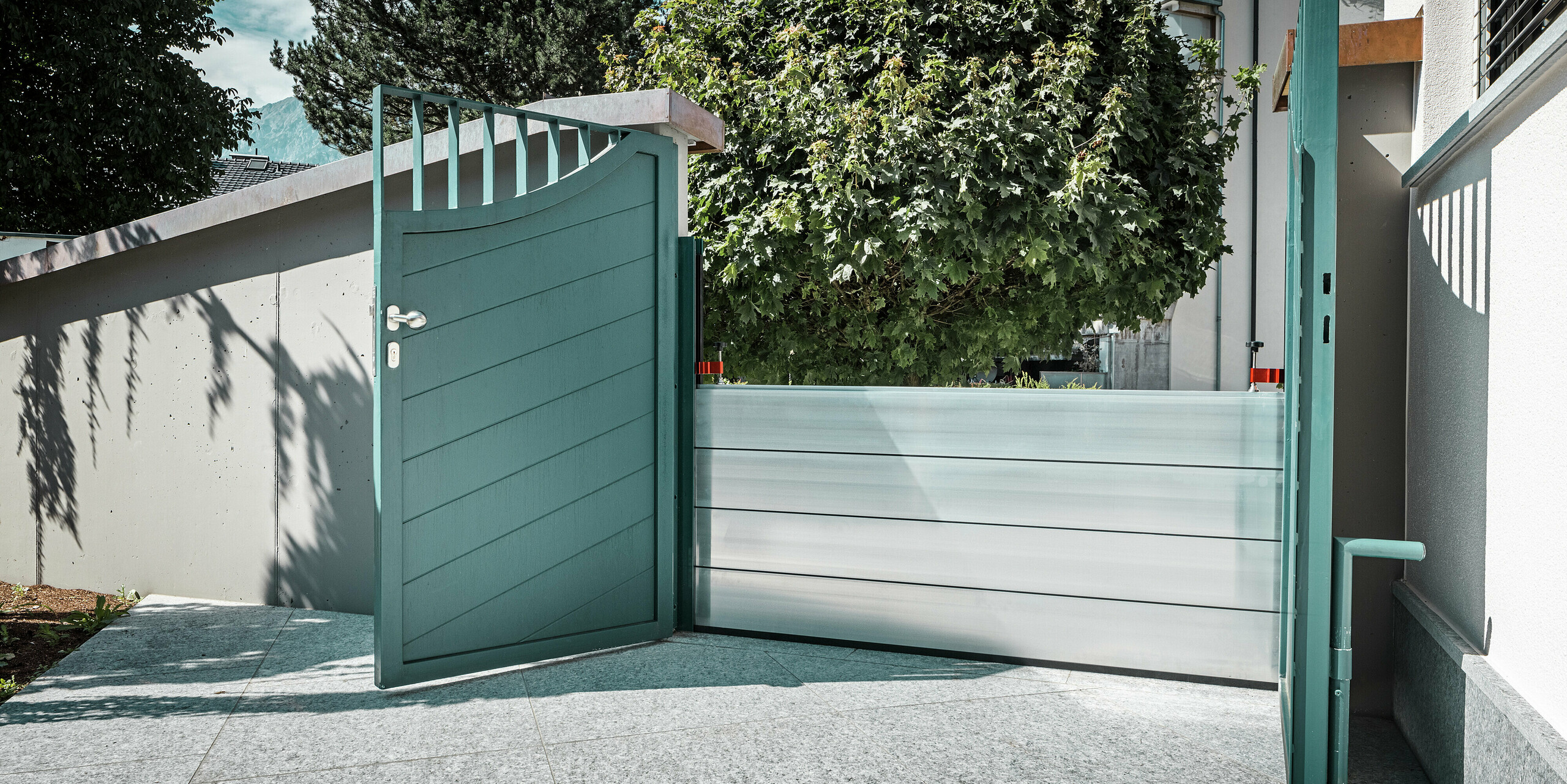 Offenes Gartentor mit integriertem PREFA Hochwasserschutzsystem vor einem Einfamilienhaus in Schwaz, Tirol. Die Aluminium Dammbalken sichern den Eingangsbereich zur Hauswand und bieten einen effektiven Objektschutz bei Überflutungen. Das System fügt sich unauffällig in die bestehende Architektur ein und unterstreicht, wie sich funktionale Sicherheit und ästhetisches Design optimal verbinden lassen.
