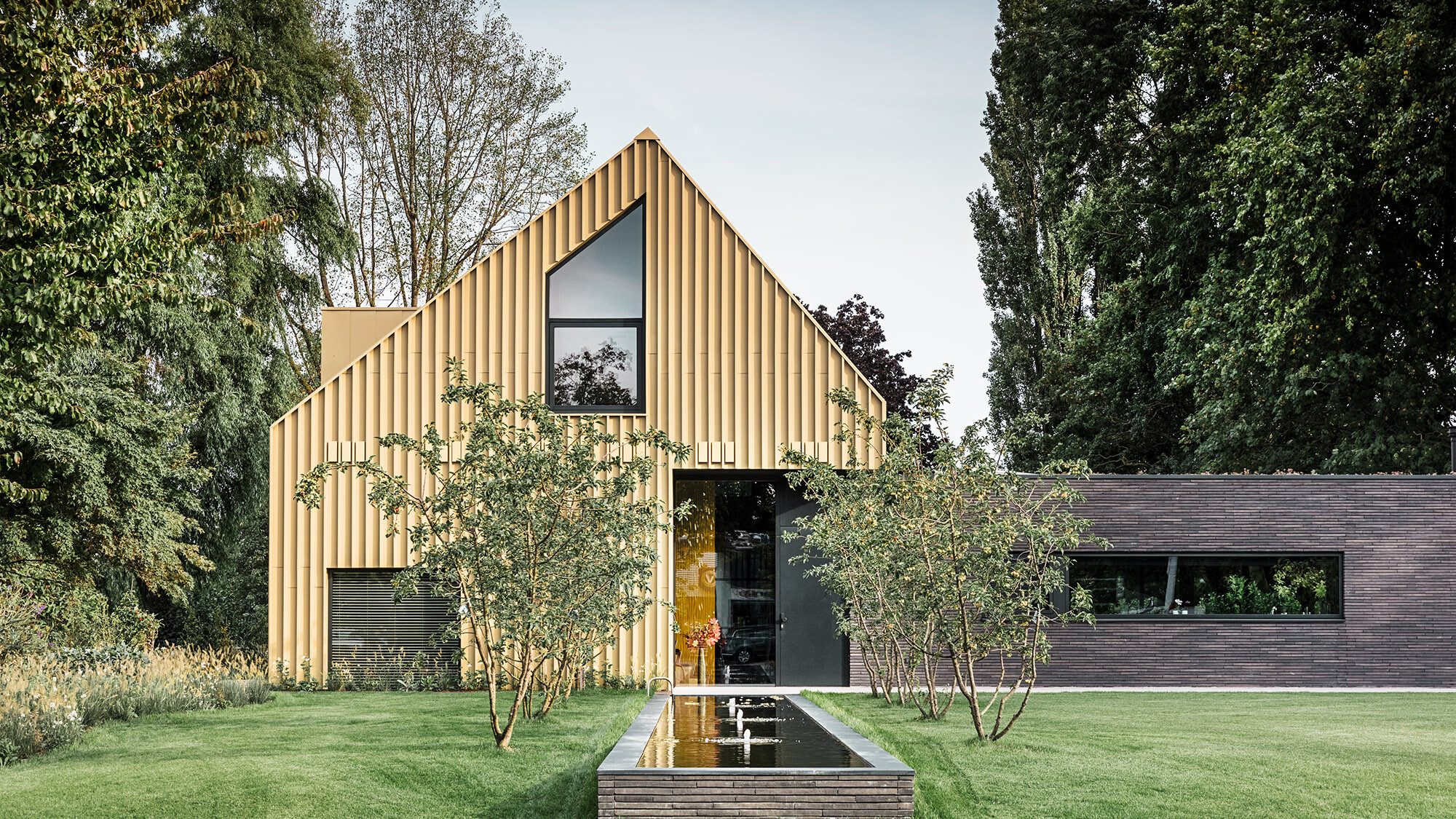 A frontal view of the detached house in Elst, which is framed by its green surroundings, the lawn with a fountain stretching out before it.