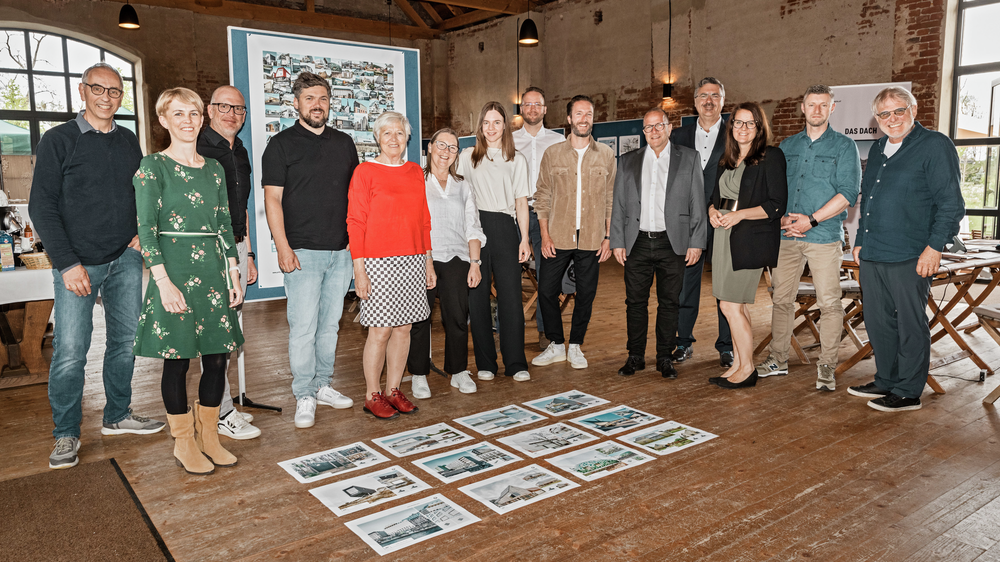 The experts and architects stand in front of the twelve selected projects and smile into the camera.