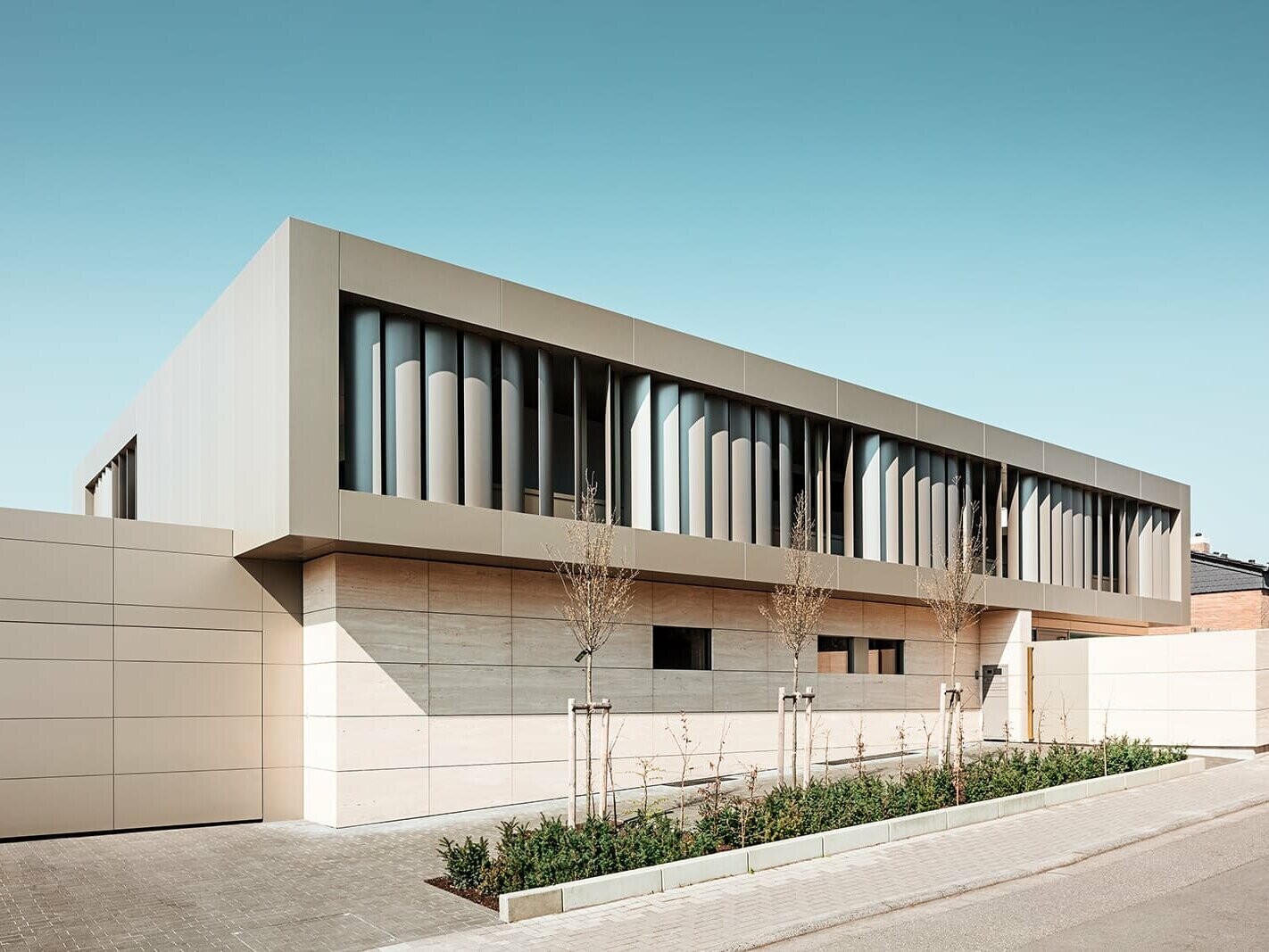 Street view, garage with bronze-coloured façade on the left, stone façade below, bronze-coloured aluminium façade with slats inside above