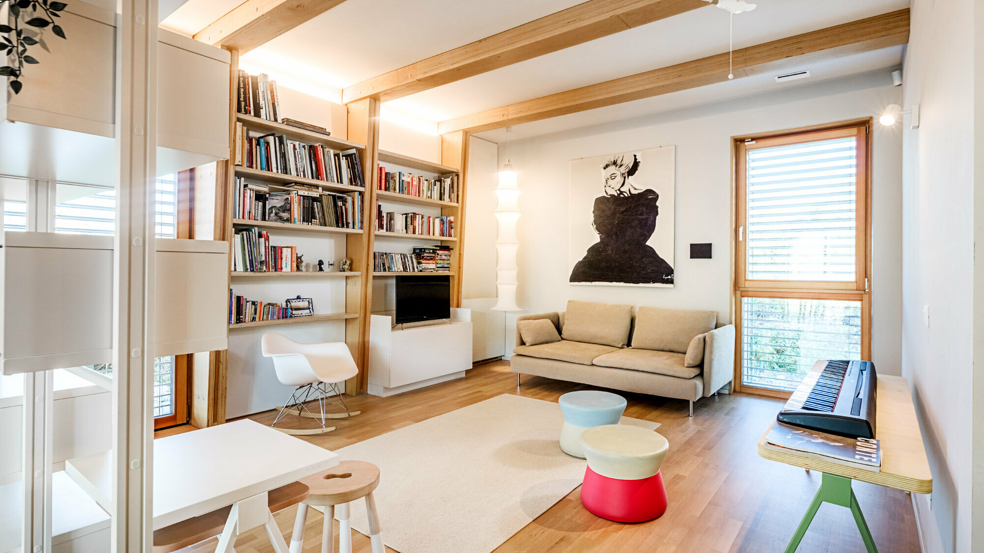 View of the interior, the bookshelf and a painting adorn the walls, a couch, keyboard, stool, table and chair are in the room.