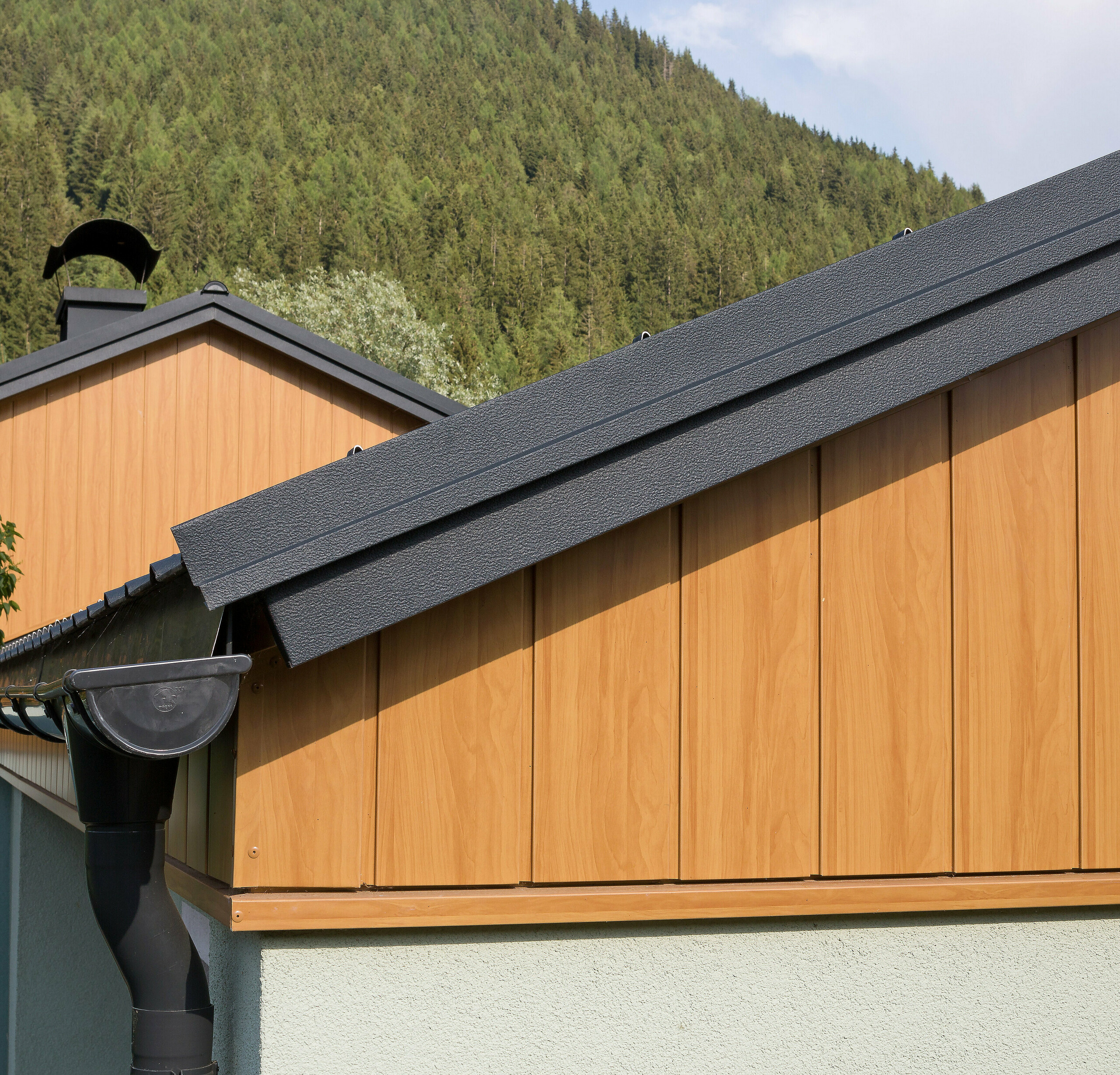 Gable cladding with aluminium sidings from PREFA in natural oak, installed vertically with a PREFA roof gutter in anthracite.