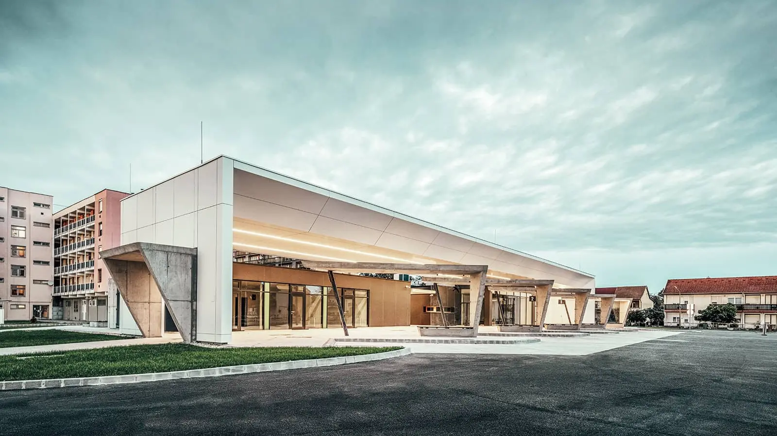 The photo shows the entire railway station at dusk. The waiting areas can be viewed from the side view. The PREFABOND composite panels on the façade in the colour pure white complement the overall picture.