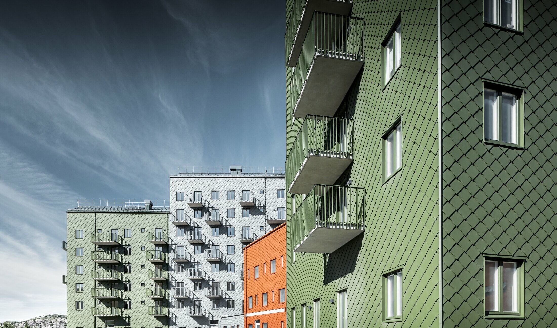 Several adjacent residential buildings clad in the PREFA 29 x 29 rhomboid façade tile in the colours brick red, olive green and light grey.