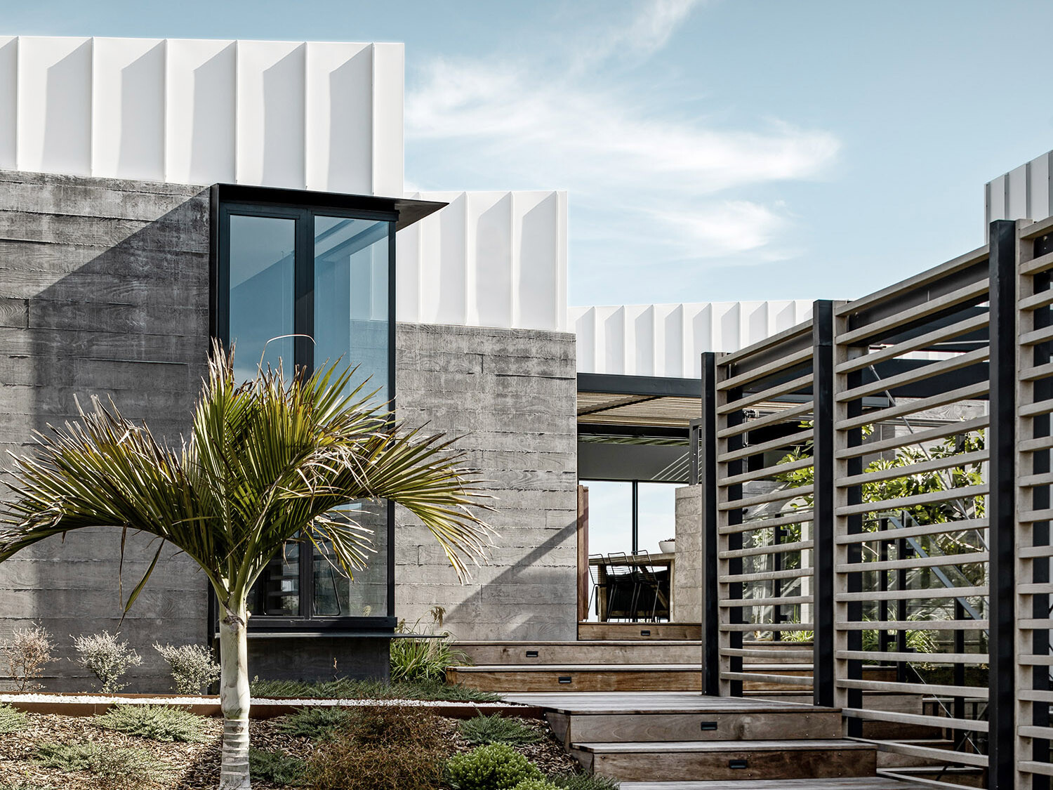 The house from the street side, with stairs leading up to the entrance and to the living area, which is visible due to the generous glazing.