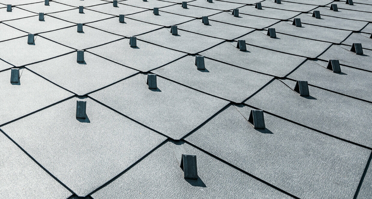 Detailed view of the PREFA rhomboid roof tile in the format 44 × 44 cm with a stucco surface in P.10 stone grey with snow guards