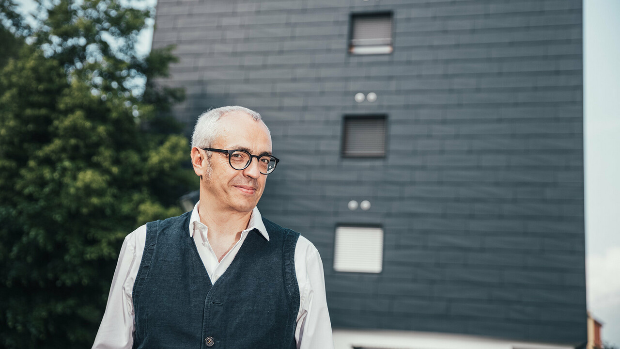 Portrait of architect Manuel Benedikter in front of the thermally renovated residential building with the anthracite-coloured PREFA façade.