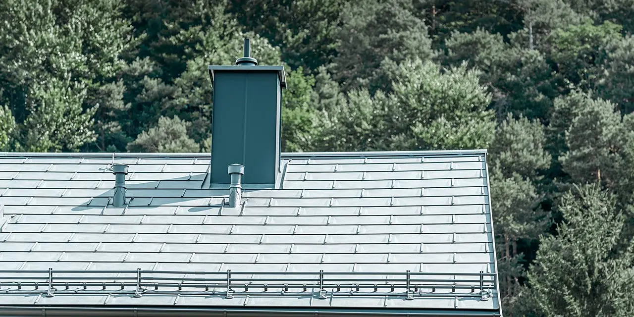 Detailed view of a gabled roof covered with the PREFA R.16 roof tile in stone grey with snow guard system, chimney surround, gutter and ventilation pipe also by PREFA