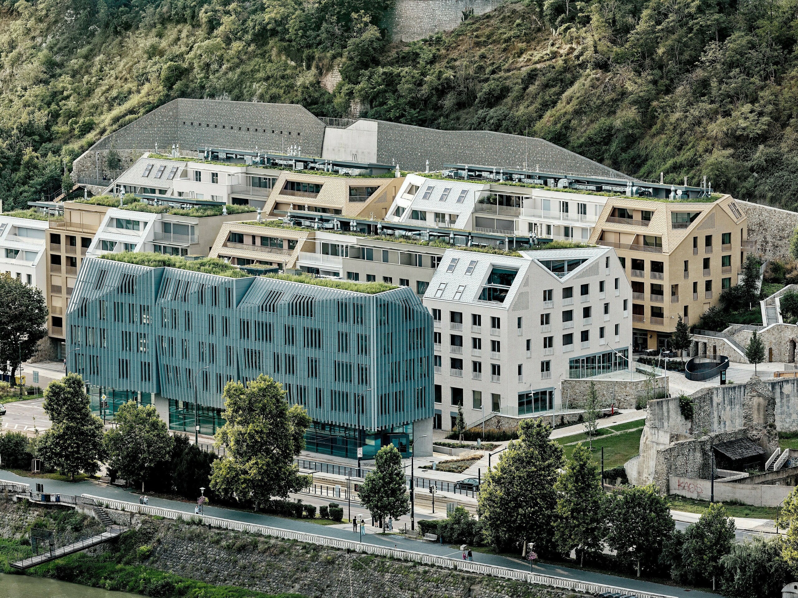 Beeindruckendes Gesamtbild des Stadtquartiers Vydrica in Bratislava am Donauufer: Die terrassierte Architektur mit begrünten Dachflächen, markanten Satteldächern und klaren Linien wird von PREFA Aluminium Dachschindeln in Prefaweiß, Sandbraun und Bronze geprägt. Die abwechslungsreiche Dachlandschaft mit integrierten Dachfenstern und präzisen Details zieht den Blick über das gesamte Ensemble. PREFA Aluminium ermöglicht filigrane, komplexe Formen und überzeugt durch Langlebigkeit, geringes Gewicht und extreme Witterungsbeständigkeit – ideal für nachhaltige, architektonisch anspruchsvolle Stadtprojekte.