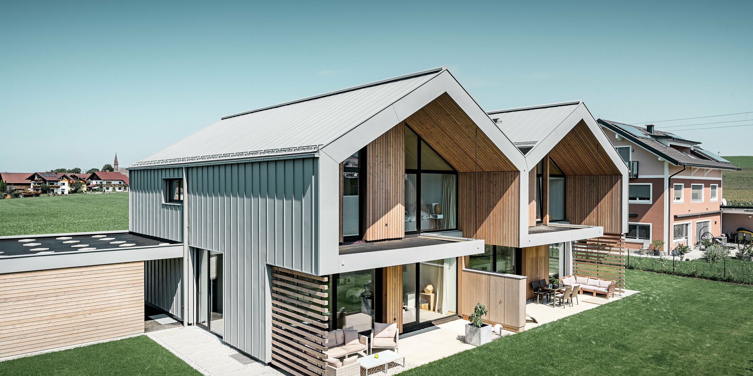 Modern semi-detached houses with PREFALZ building shell, roof and façade are clad with PREFALZ in patina grey incl. square downpipe
