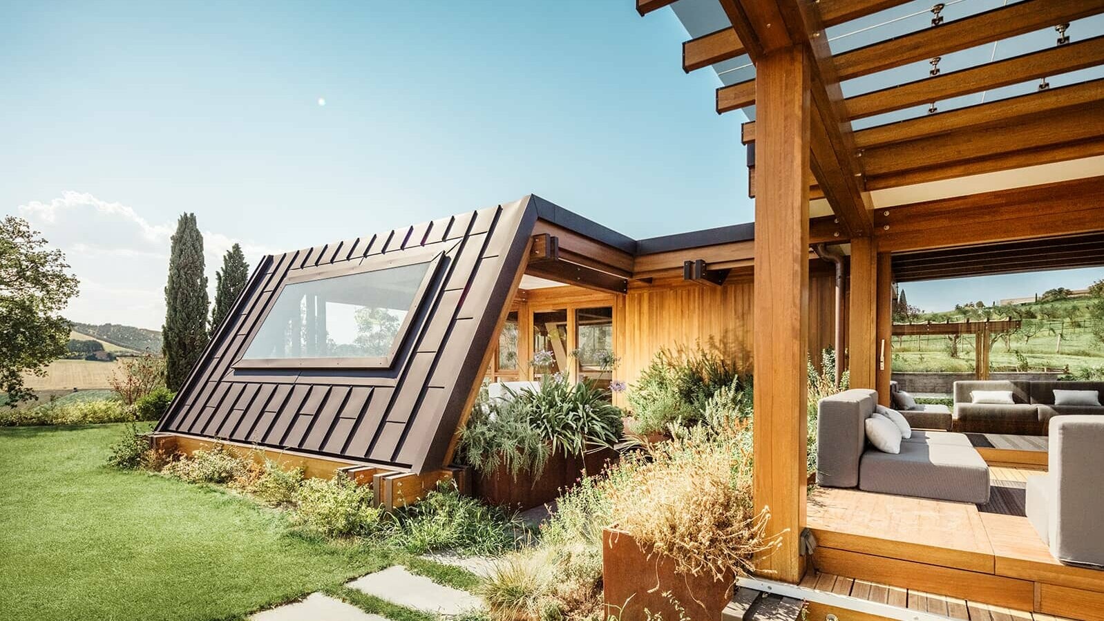 A picture of the Pagano show house in Italy. The chill out area on the left side can be seen. The Prefalz façade in nut brown is illuminated by the sun.