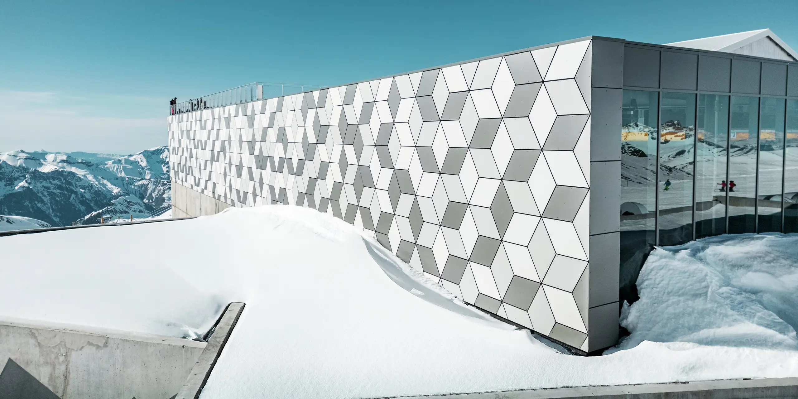 Die Bergstation der Seilbahn in Les Deux Alpes präsentiert sich mit einer atemberaubenden Fassade aus PREFABOND Aluminium-Verbundplatten, die in einem auffälligen Rautenmuster angeordnet sind. Die Platten in den Farben Weiß und Grau fügen sich nahtlos in die verschneite Berglandschaft ein und reflektieren das klare, alpine Licht. Diese innovative Fassadengestaltung vereint ästhetische Raffinesse und hohe Widerstandsfähigkeit gegen extreme Witterungsbedingungen.