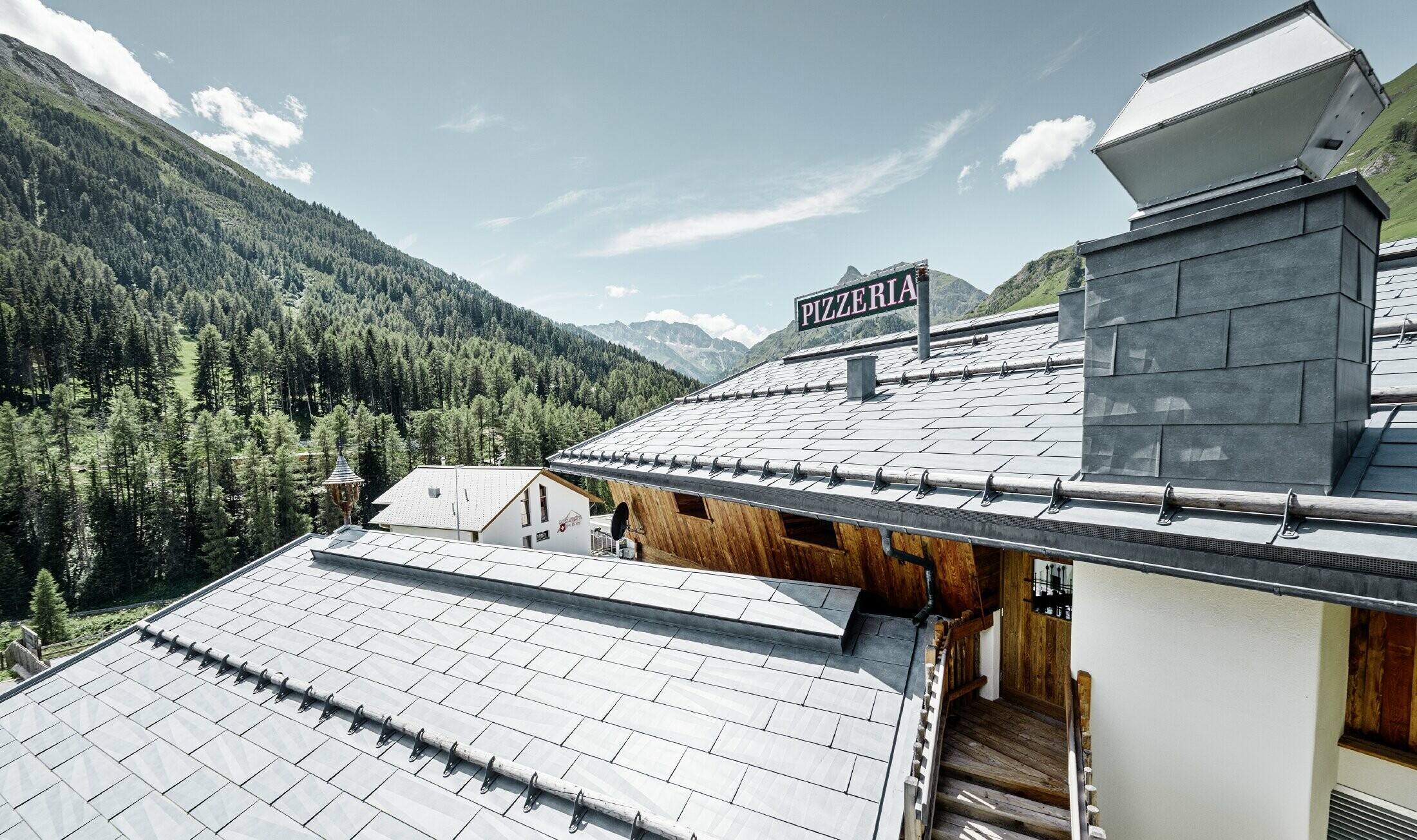 Restaurant Almrausch with a mountainous backdrop and a PREFA roof with FX.12 roof panels in stone grey and mountain snow guard brackets
