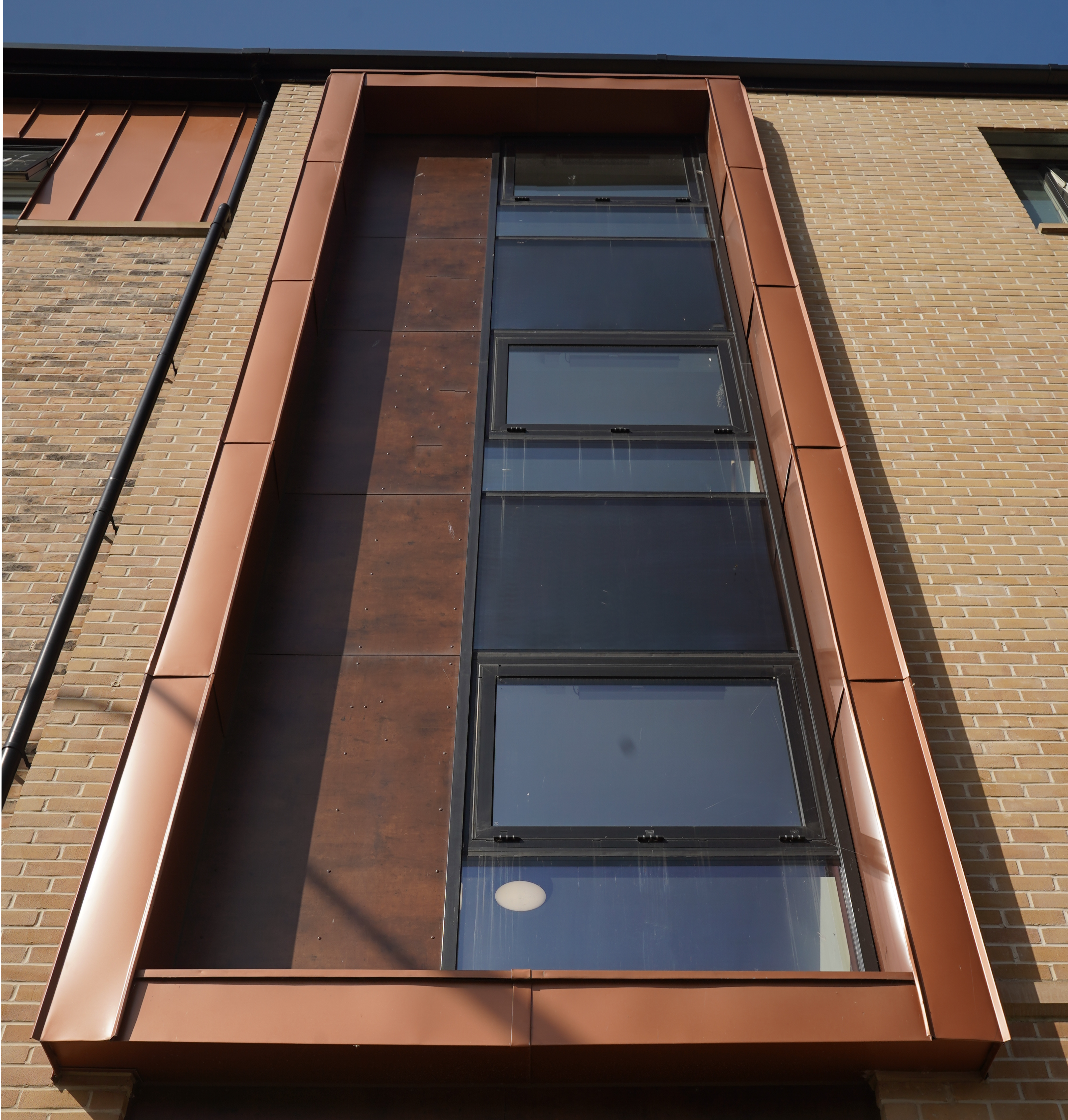 Close-up of a window area on the façade of a residential development on Nethan Street in Glasgow, framed by FALZONAL in New Copper. This high quality PREFA aluminium product complements the clean glass architecture with its warm copper colour, creating a visual link between modern construction and traditional materials. The FALZONAL finish emphasises the precise and sophisticated design of the residential building.